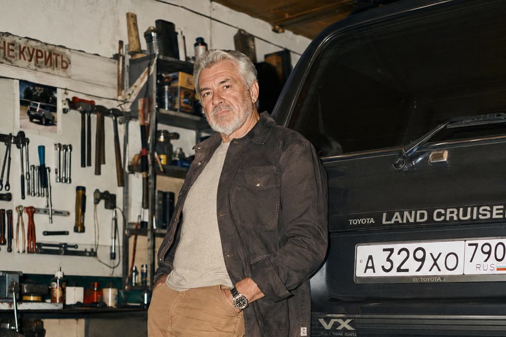 Седой мужчина в гараже у Toyota Land Cruiser, на стене инструменты и табличка «Не курить»